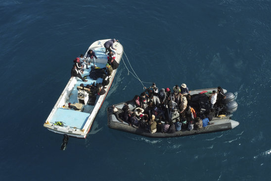 Vue aérienne d'un bateau de migrants entrant dans le port de Garaboulli, après avoir été secourus en mer par les gardes-côtes, le 26 avril 2023 en Libye (Crédit photo : AFP / Mahmud Turkia)