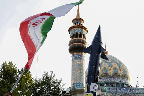 Des Iraniens brandissent un drapeau et la maquette d'un missile après après l'attaque de missiles et de drones iranien (Crédit photo : AFP / ATTA KENARE)