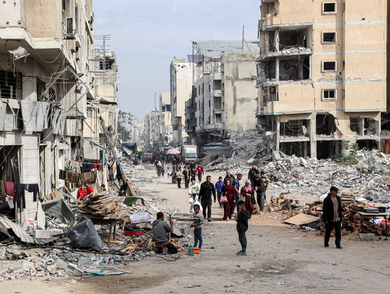 Des personnes marchent devant les décombres de bâtiments effondrés et endommagés dans une rue de la ville de Gaza, le 11 décembre 2024 (Crédit photo : AFP / Omar AL-QATTAA)